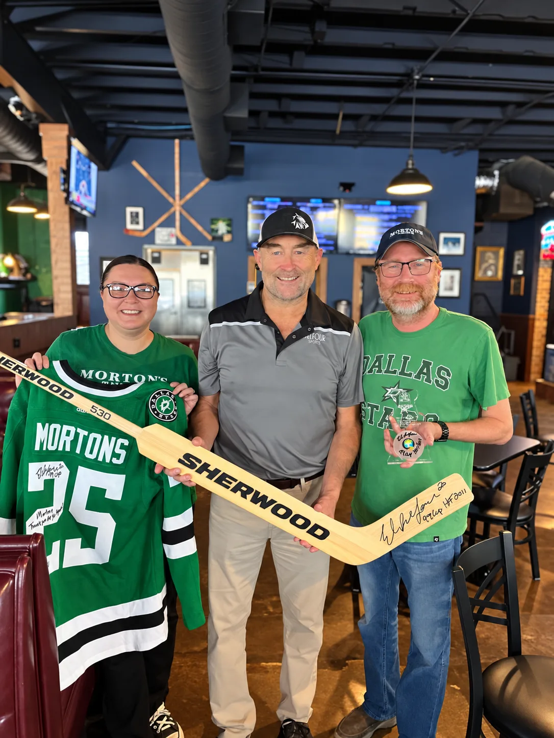 Monika Morton, Dallas Stars Stanley Cup goalie Eddy "The Eagle" Belfour, and Jimmy Morton with a Morton's Stars jersey and hockey stick at Morton's Tavern in Fort Worth