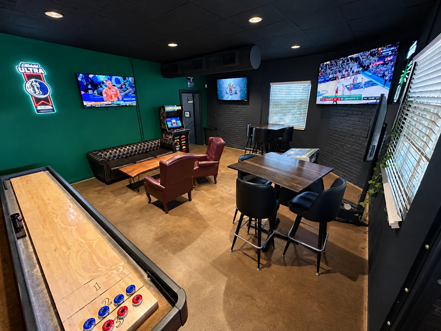 The back room game room with a shuffleboard table, Golden Tee, lounge seating, and TVs at Morton's Tavern in Fort Worth